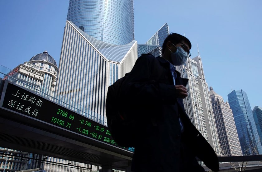 FILE PHOTO: A pedestrian wearing a face mask walks near an overpass with an electronic board showing stock information, following an outbreak of the coronavirus disease (COVID-19), at Lujiazui financial district in Shanghai, China March 17, 2020. REUTERS/Aly Song