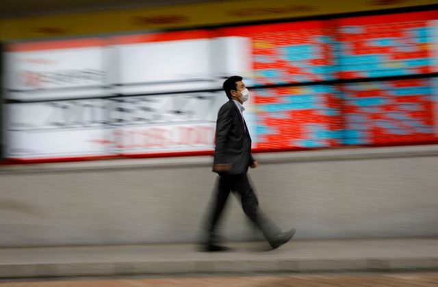 FILE PHOTO: A man wearing a protective face mask, following the coronavirus disease (COVID-19) outbreak, walks in front of a stock quotation board outside a brokerage in Tokyo, Japan, May 18, 2020. REUTERS/Kim Kyung-Hoon