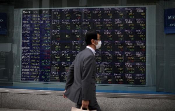 FILE PHOTO: A man wearing protective face mask, following an outbreak of the coronavirus disease (COVID-19), walks in front of a stock quotation board outside a brokerage in Tokyo, Japan, March 10, 2020. REUTERS/Stoyan Nenov