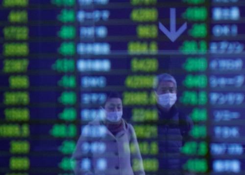 Passersby wearing protective face masks, following an outbreak of the coronavirus, are reflected on a screen displaying stock prices outside a brokerage in Tokyo, Japan March 6, 2020.