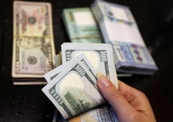 FILE PHOTO: A woman counts U.S. dollar banknotes as Lebanese pounds are pictured in the background at a currency exchange shop in Beirut, Lebanon April 3, 2020. REUTERS/Mohamed Azakir